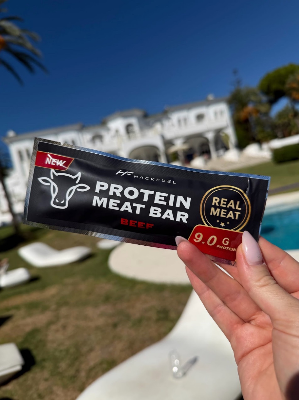 A hand holding a HackFuel beef bar in a sunny Marbella garden