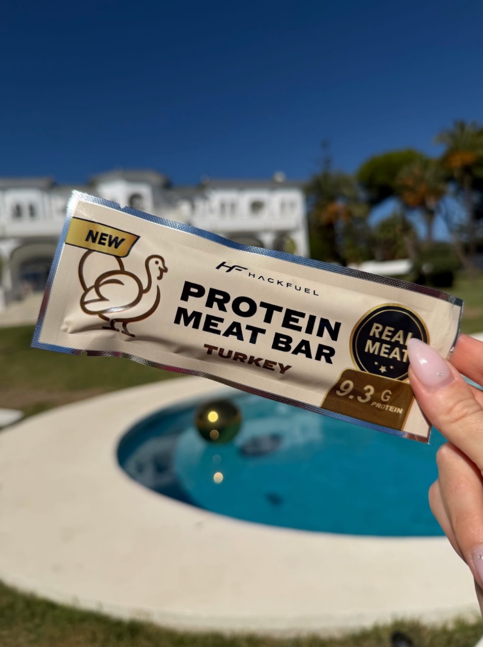 A hand holding a HackFuel turkey bar in front of a pool